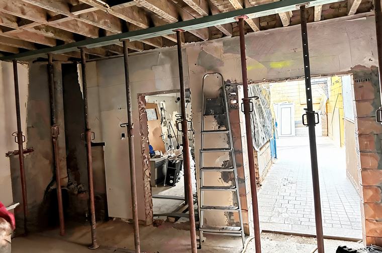 Het veilig opvangen van de plafondconstructie met stempels (schoren) en een stalen draagbalk om de binnenmuur en het raamkozijn definitief weg te breken.